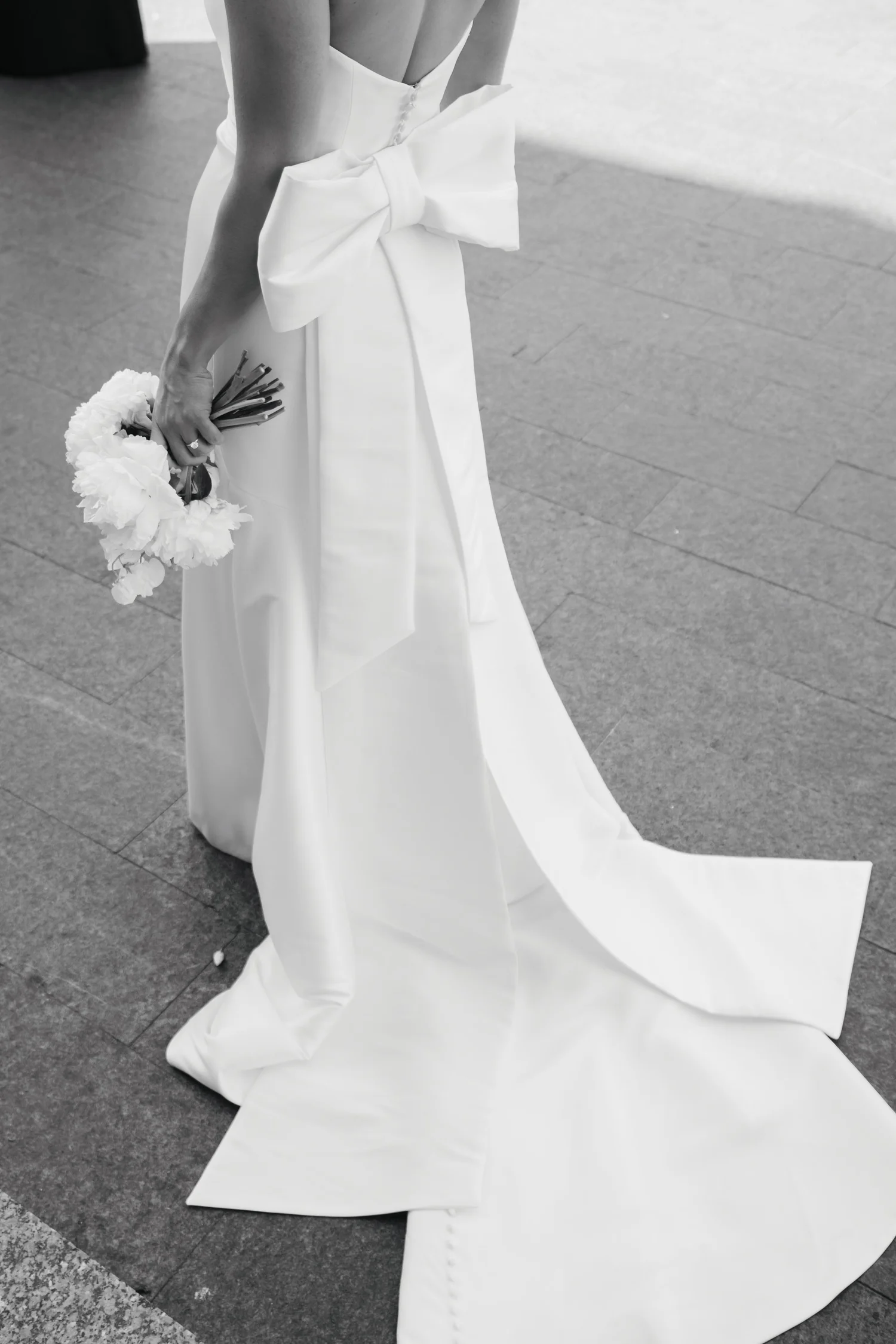 back view of a woman standing in white wedding dress holding a bouquet